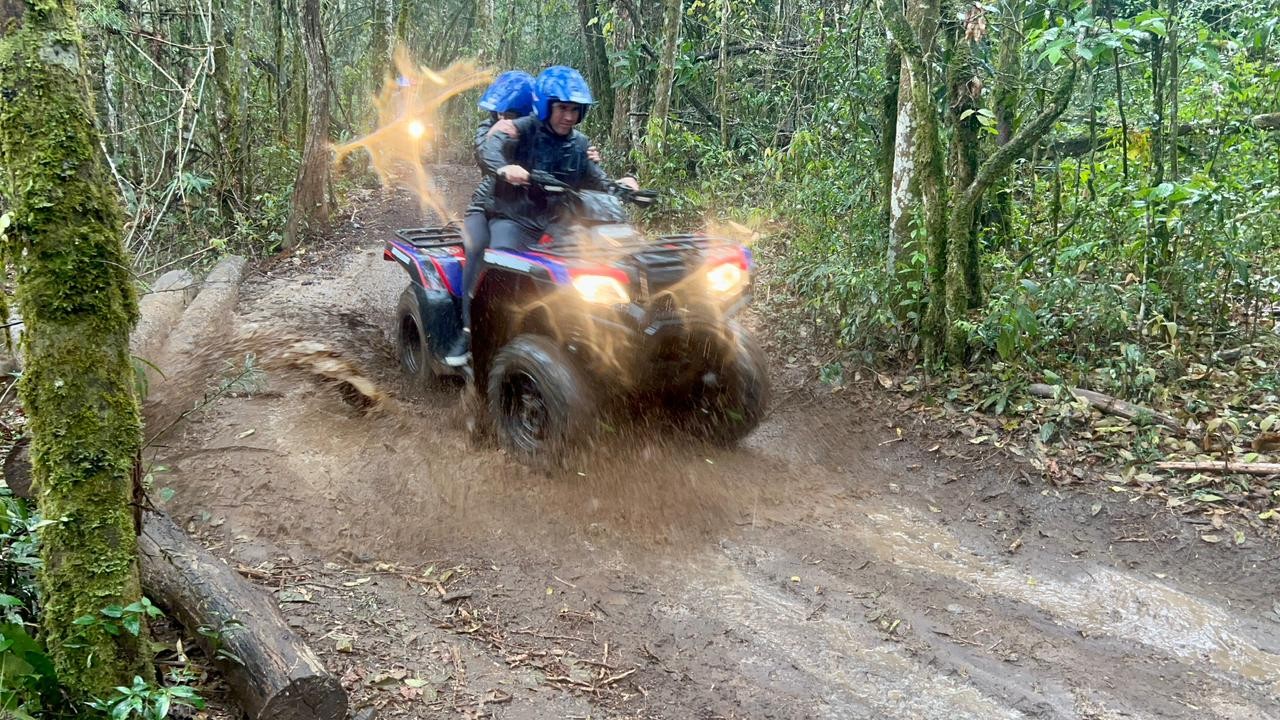 Quadriciclos seguem pela trilha na mata, com participantes usando capacete.