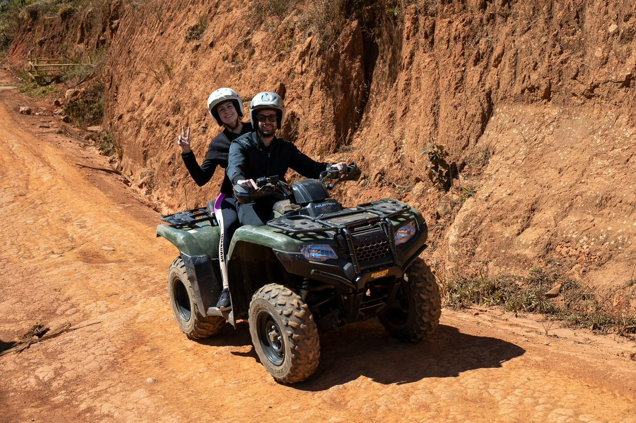 Duas pessoas de capacete no mesmo quadriciclo, em uma trilha de terra.